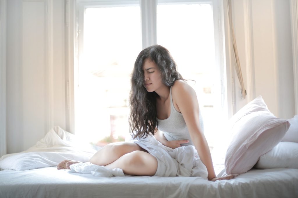 A woman in bed experiencing stomach ache.