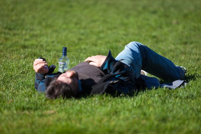 Drunk person lying on the grass with an empty bottle next to him