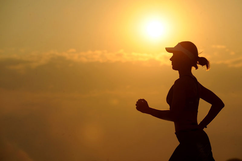 A silhouette of a woman running with the sun in the background.