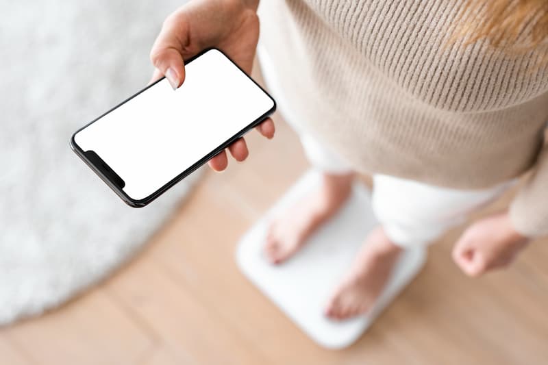 A woman standing on a weight and holding a smartphone.